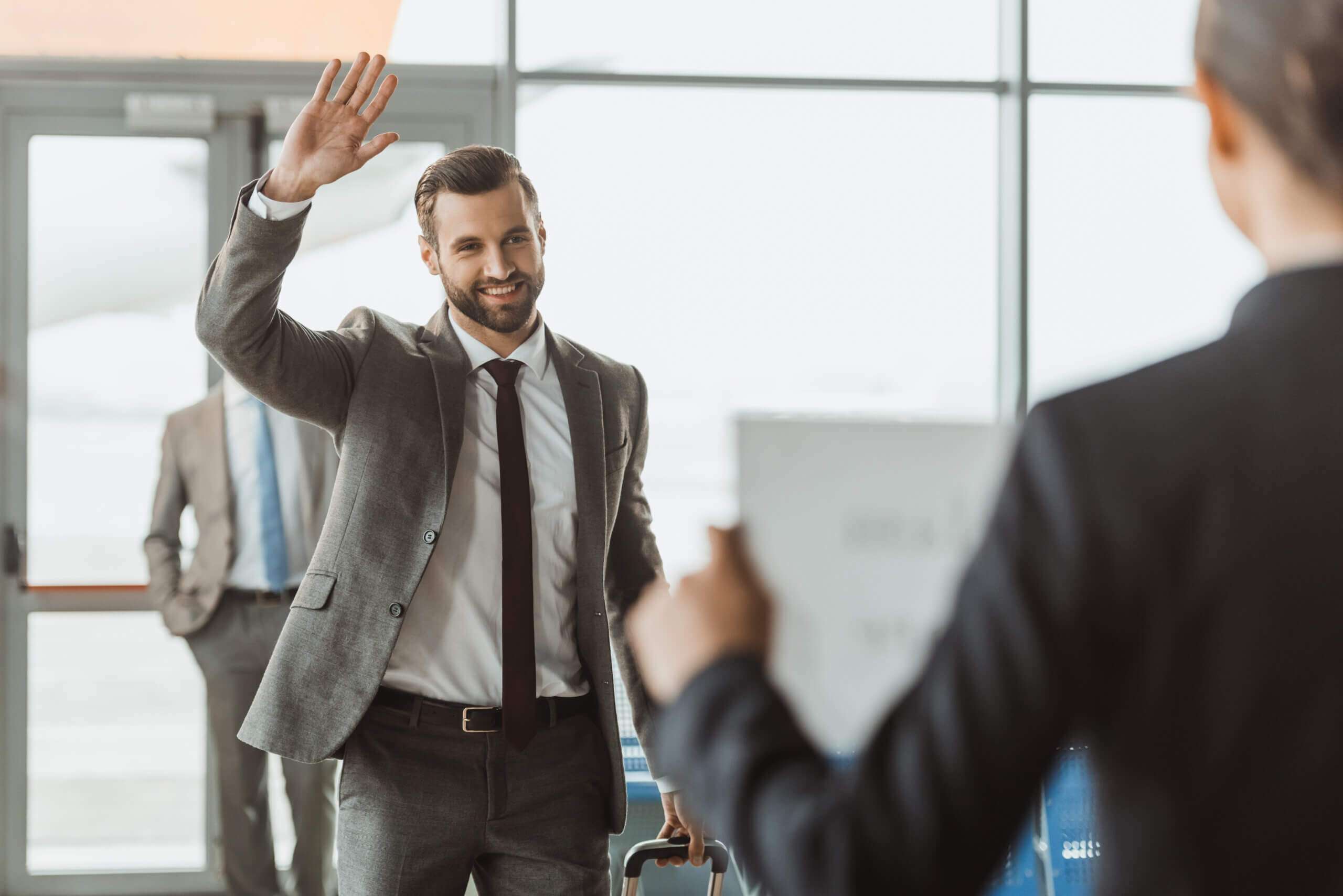 Chauffeur in suit waving to client at airport meet and greet service.