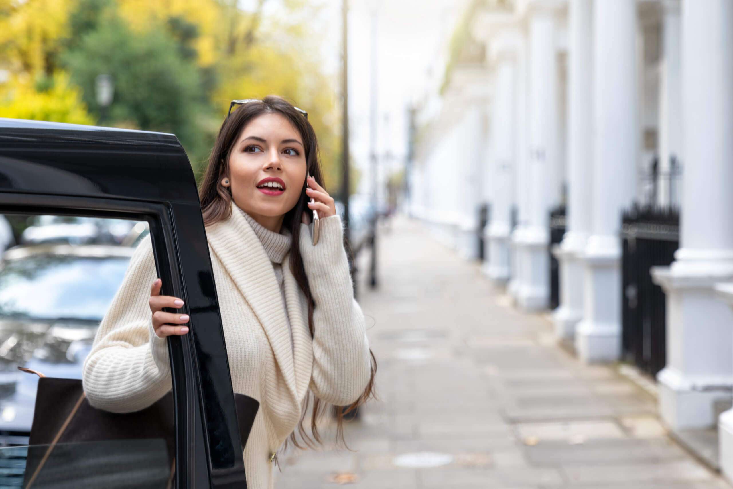 Woman exiting chauffeur-driven car in London, talking on phone.