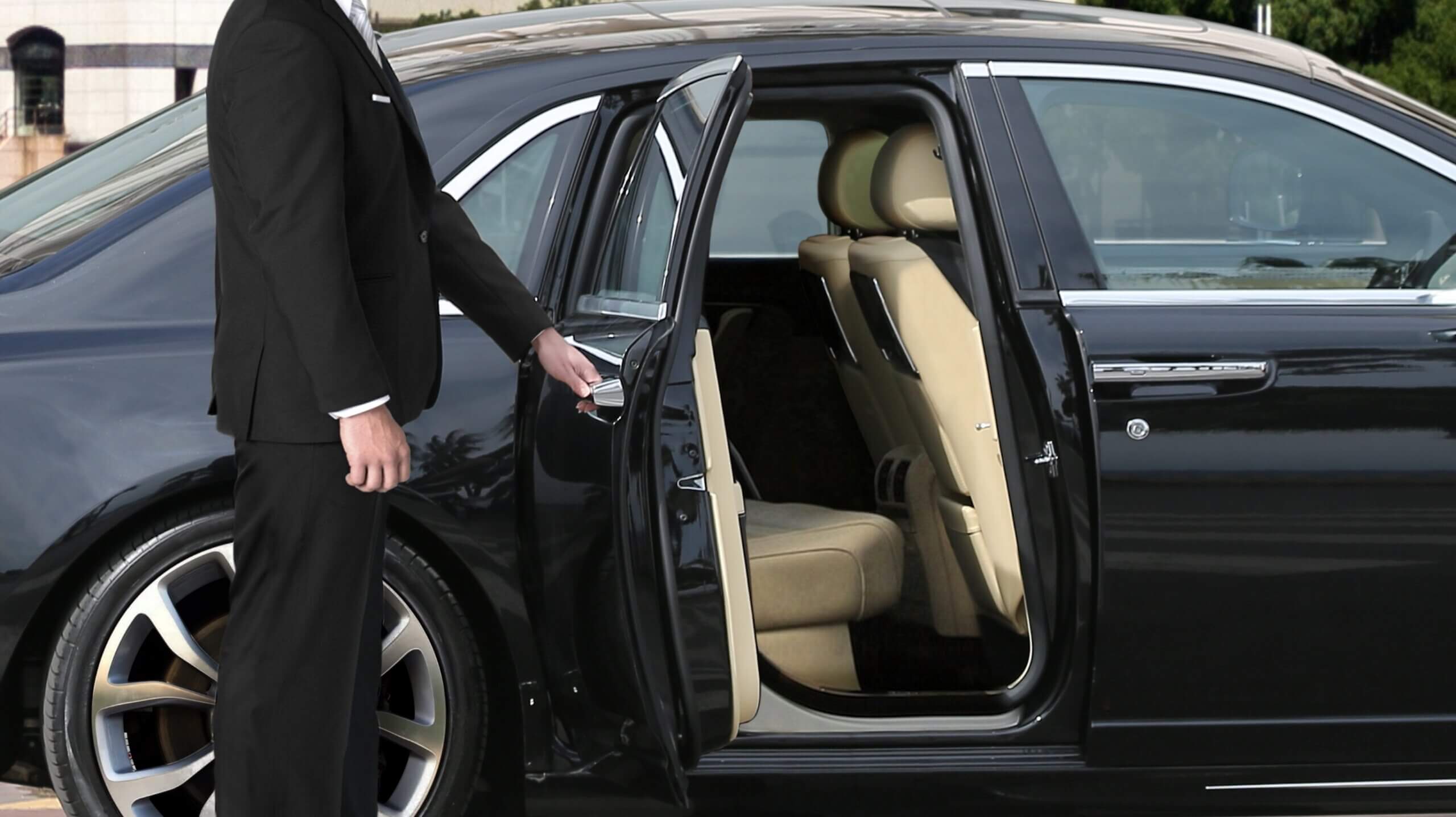 Chauffeur opening car door for passenger, luxury chauffeur service, REAL Transfers.