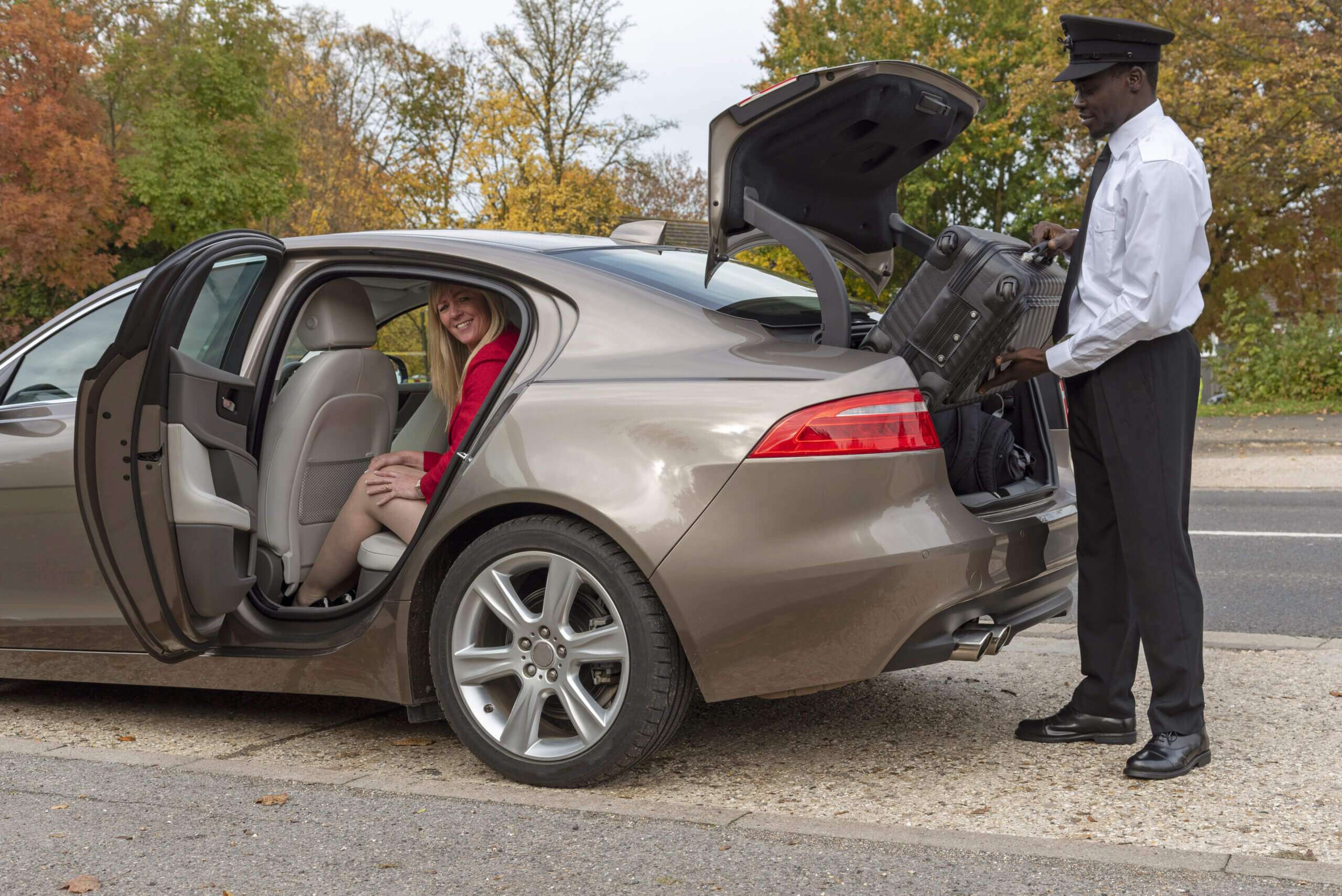Chauffeur assisting passenger with luggage into luxury executive car for a stylish arrival.