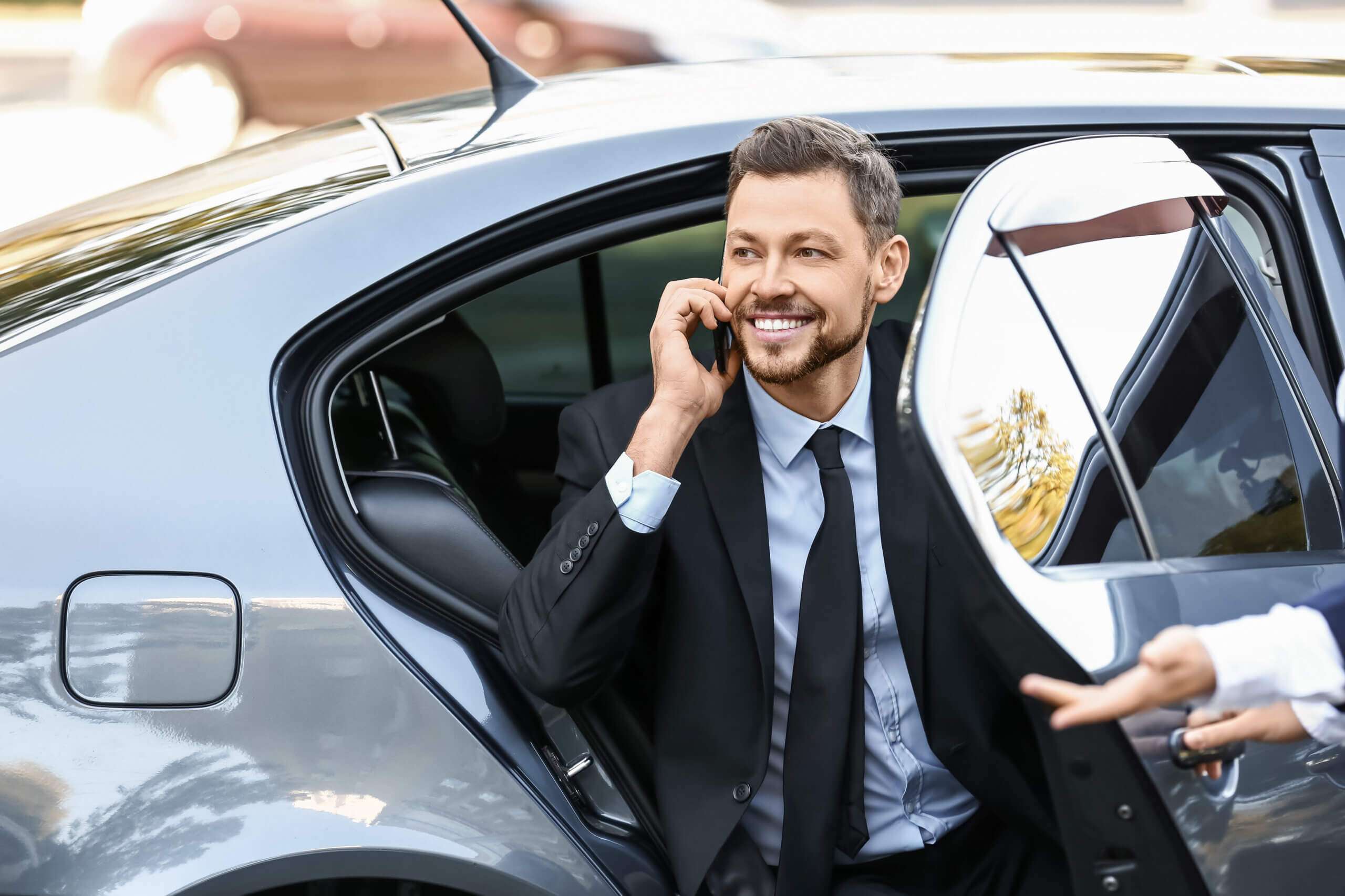 Business executive exiting chauffeur-driven luxury vehicle and talking on phone.