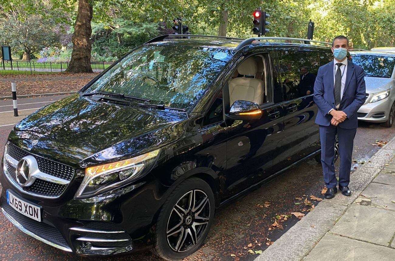 Chauffeur in London standing beside a black Mercedes luxury car and cruise transfer vehicle.