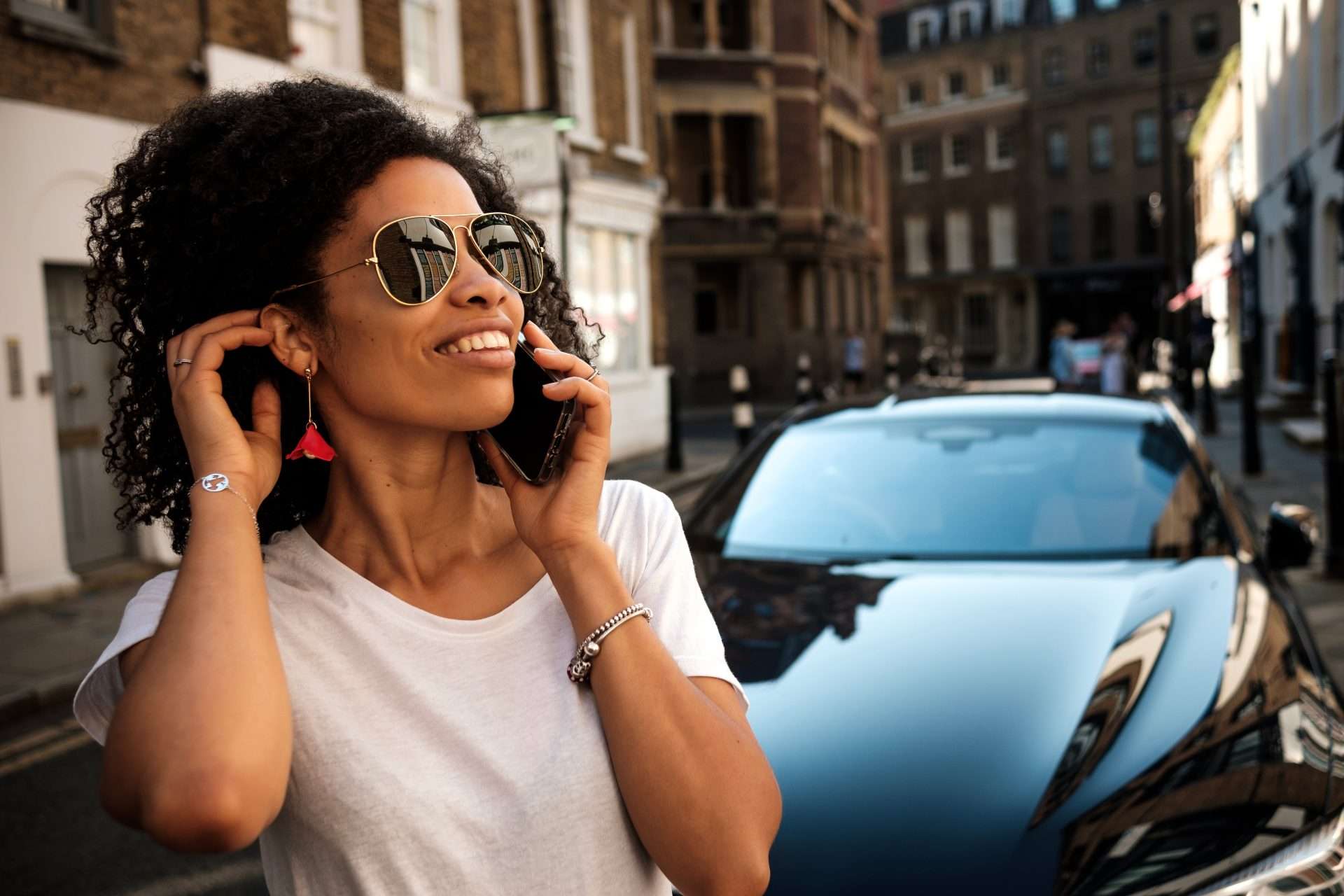 Stylish woman on phone near luxury car in London, chauffeur service transportation.