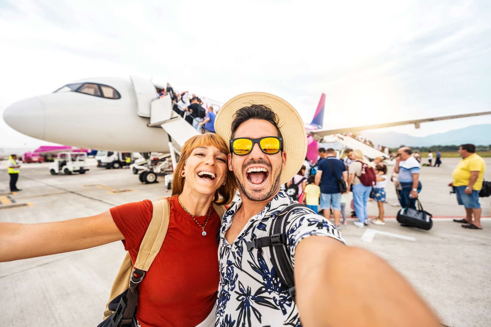 Couple taking selfie near airplane at airport, luxury summer holiday transfers.