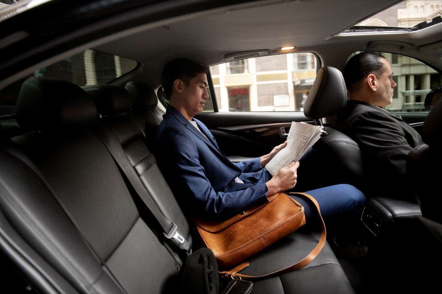 Business traveler in luxury chauffeur car, reading documents during REAL Transfers service.